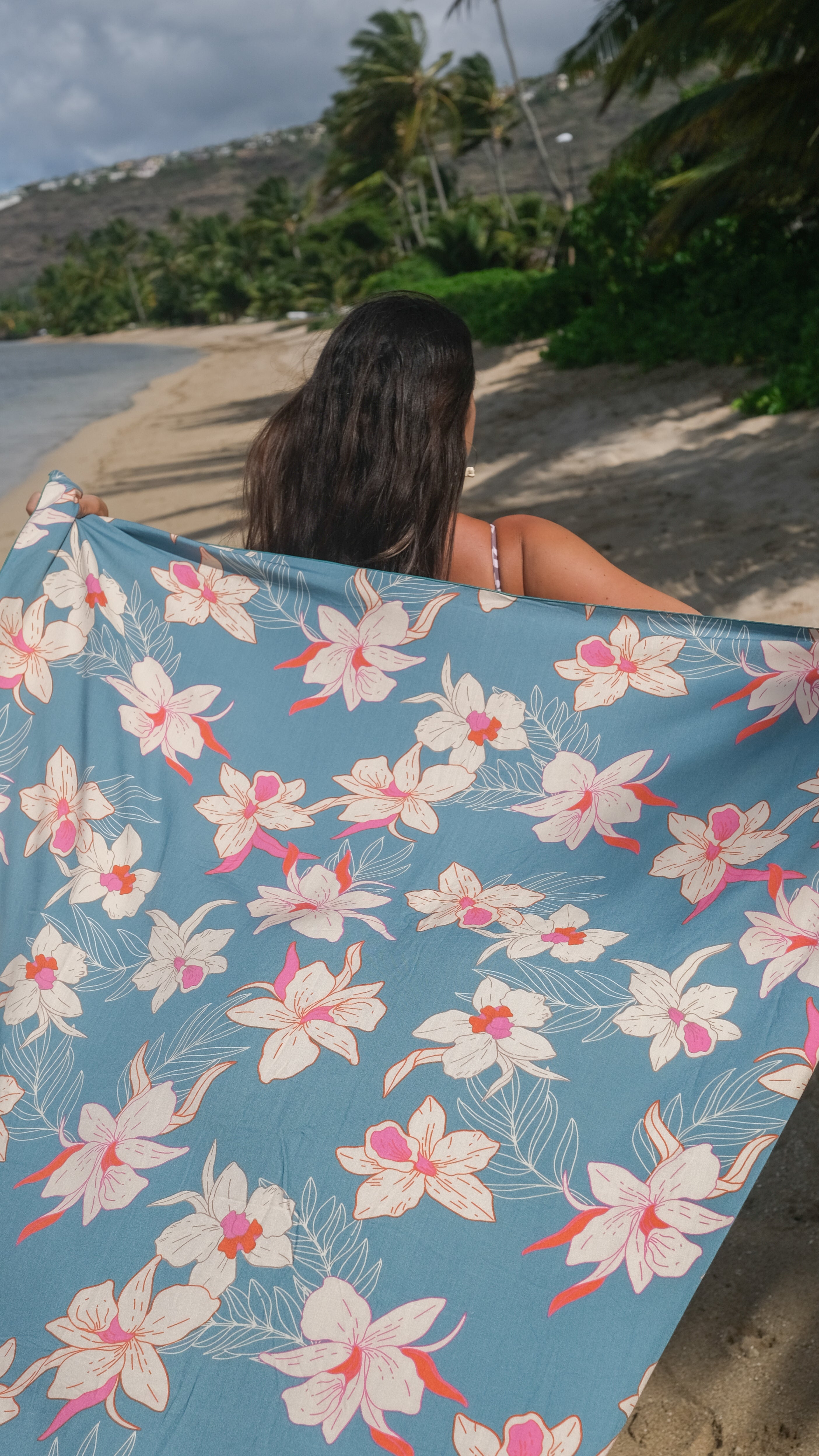 woman holding a pareo in teal color with cream colored orchids