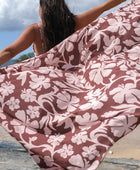 woman with brown hair holding a pareo with blush pink and brown hibiscus print 
