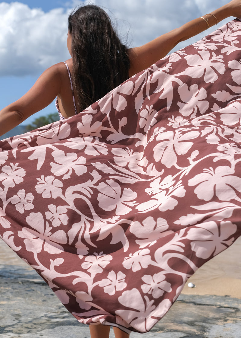 woman with brown hair holding a pareo with blush pink and brown hibiscus print 