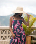 Woman wearing a dark blue sundress featuring pink ginger flowers and lei.