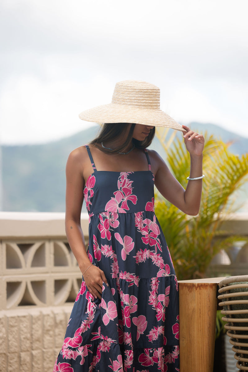 Woman wearing a dark blue sundress featuring pink ginger flowers and lei.