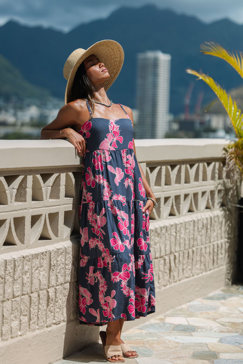 Woman wearing a dark blue sundress featuring pink ginger flowers and lei.