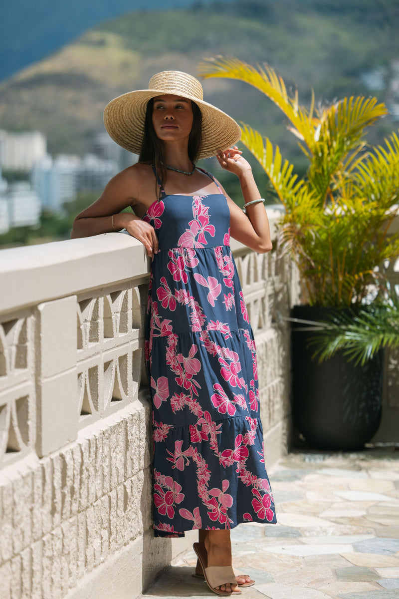 Woman wearing a dark blue sundress featuring pink ginger flowers and lei.