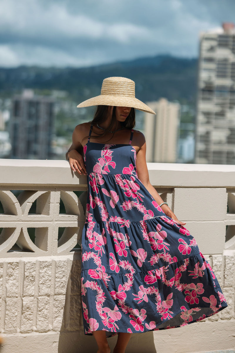 Woman wearing a dark blue sundress featuring pink ginger flowers and lei.