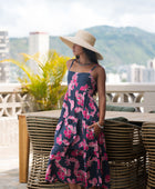 Woman wearing a dark blue sundress featuring pink ginger flowers and lei.