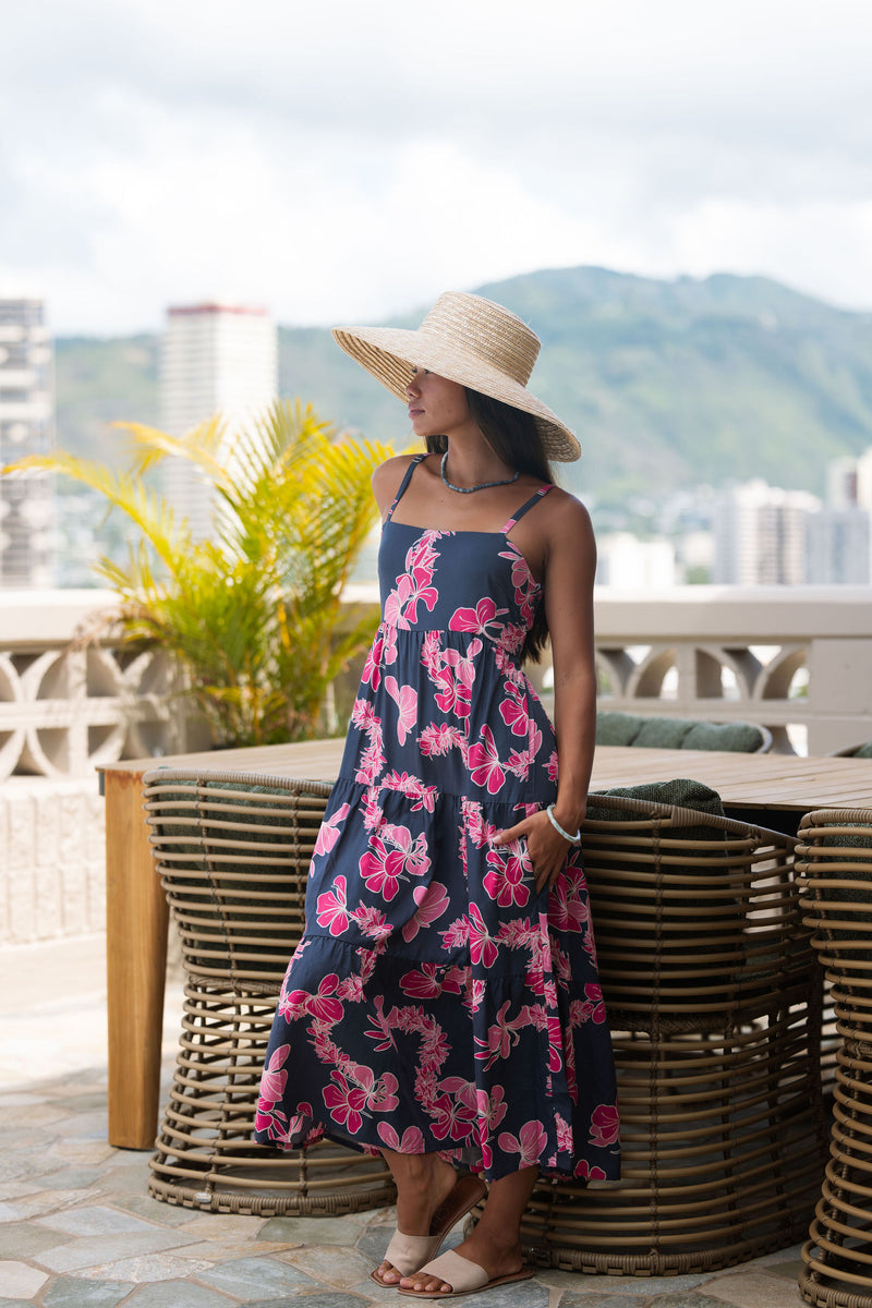 Woman wearing a dark blue sundress featuring pink ginger flowers and lei.