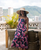 Woman wearing a dark blue sundress featuring pink ginger flowers and lei.