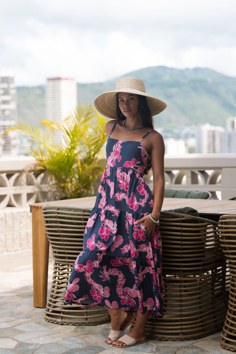 Woman wearing a dark blue sundress featuring pink ginger flowers and lei.