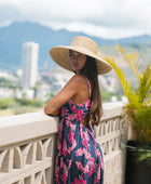 Woman wearing a dark blue sundress featuring pink ginger flowers and lei.