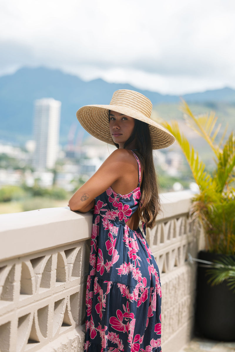 Woman wearing a dark blue sundress featuring pink ginger flowers and lei.