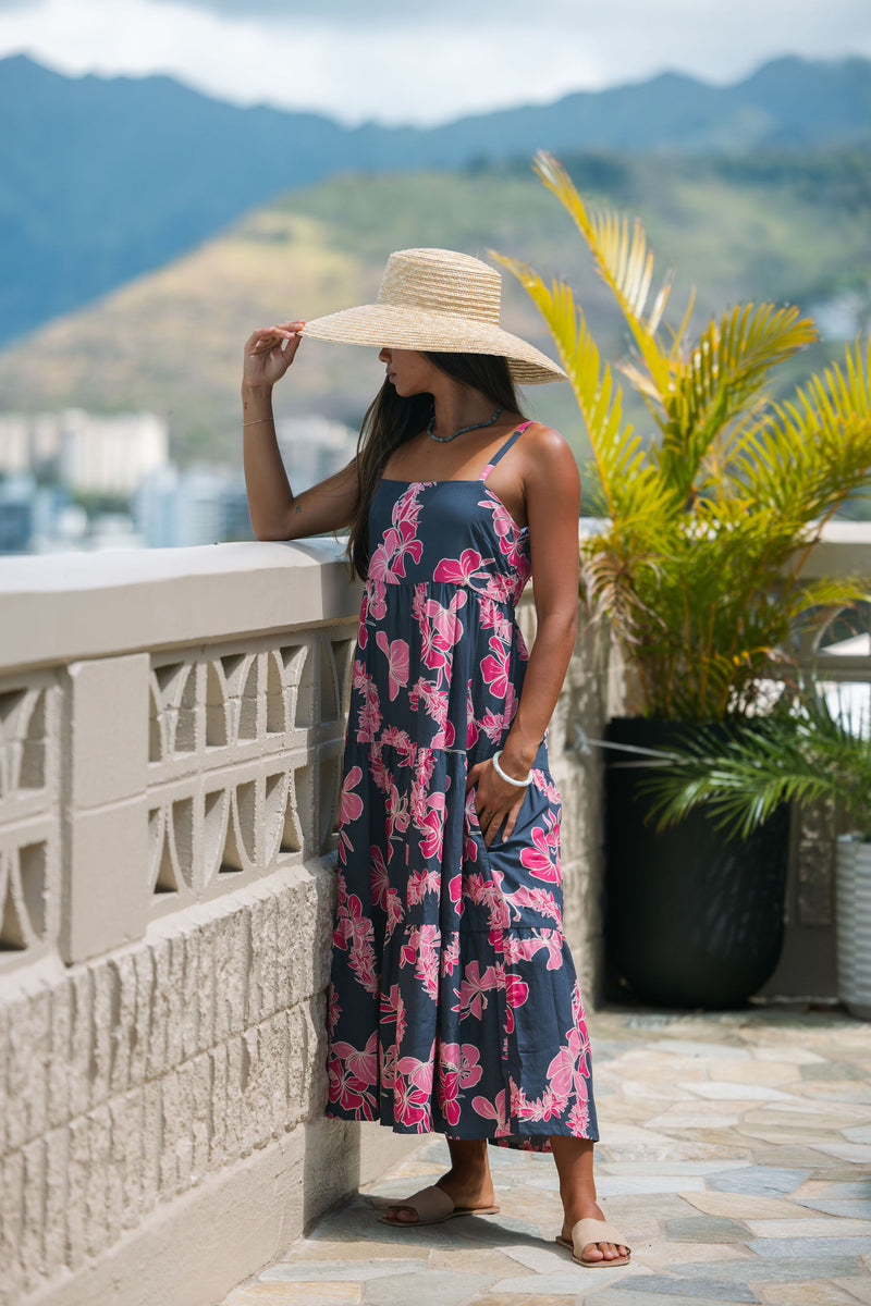 Woman wearing a dark blue sundress featuring pink ginger flowers and lei.