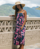 Woman wearing a dark blue sundress featuring pink ginger flowers and lei.