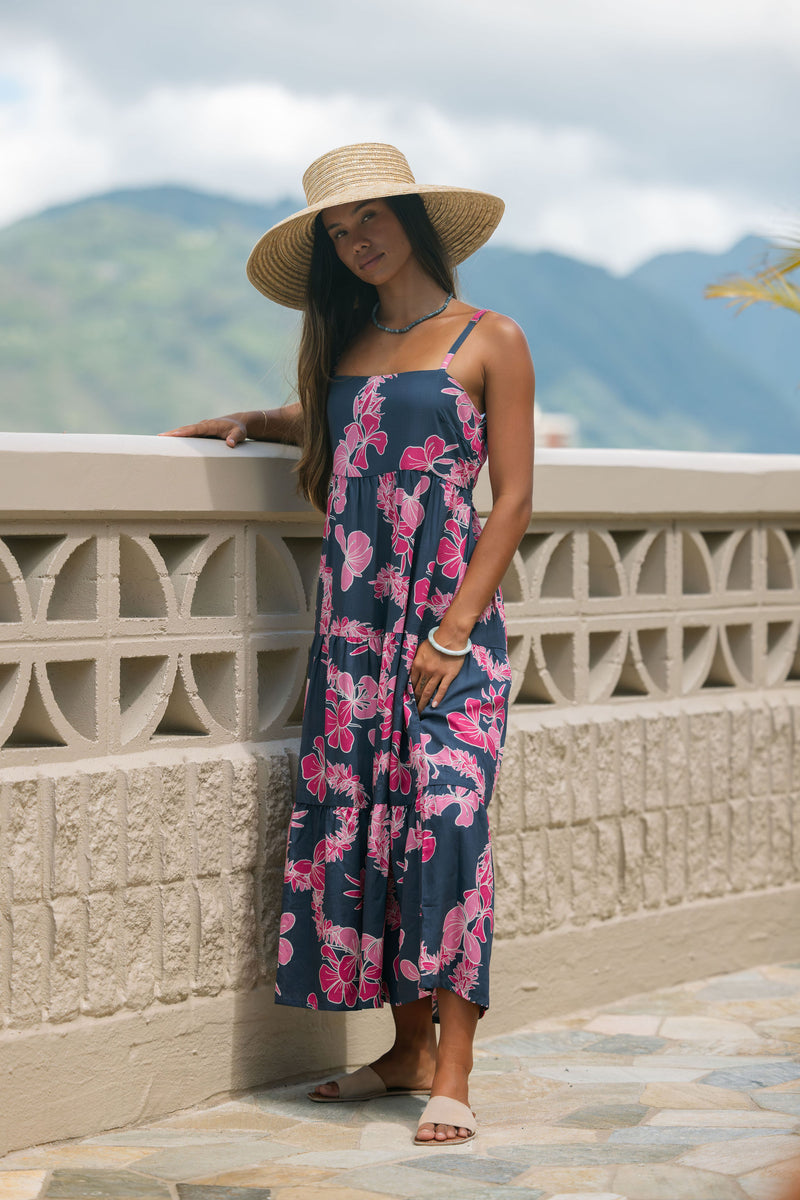 Woman wearing a dark blue sundress featuring pink ginger flowers and lei.