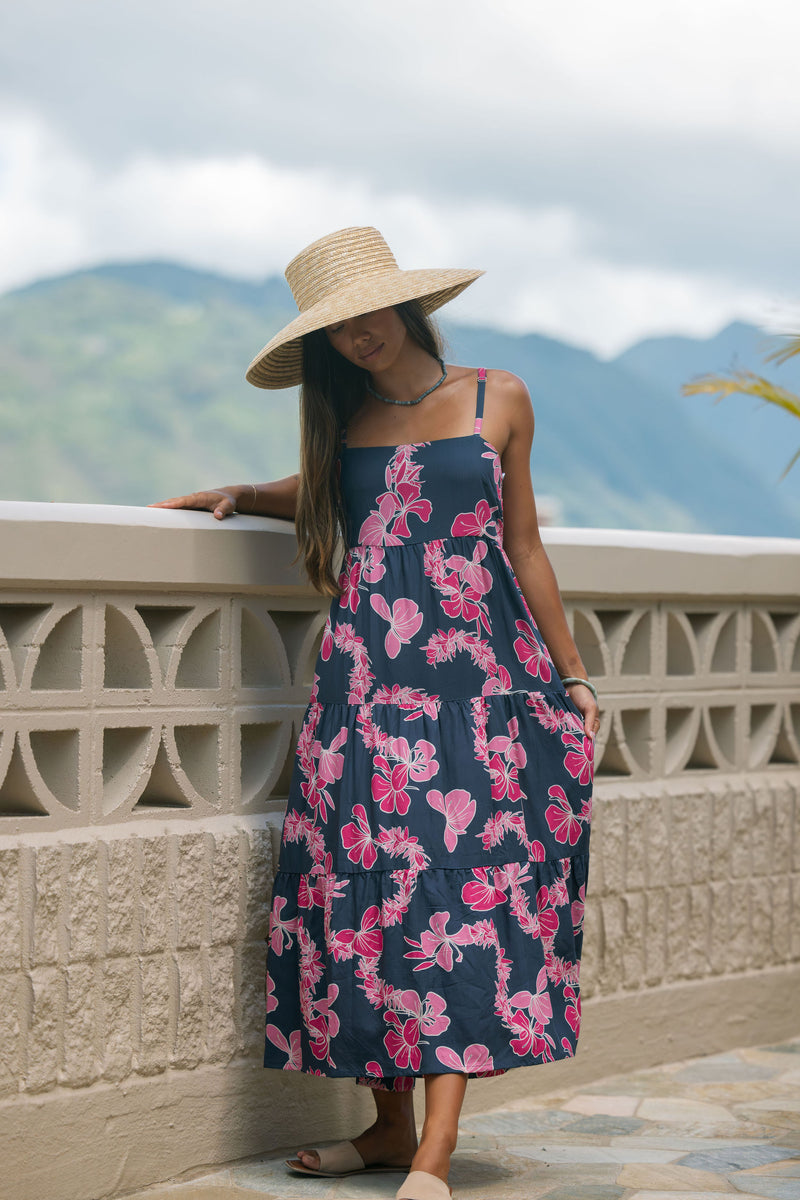 Woman wearing a dark blue sundress featuring pink ginger flowers and lei.