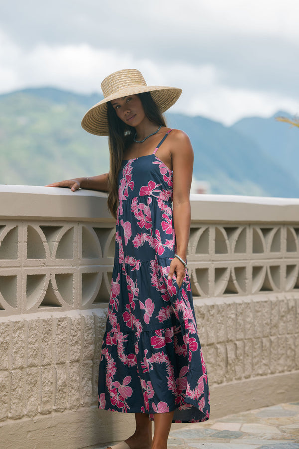 Woman wearing a dark blue sundress featuring pink ginger flowers and lei.