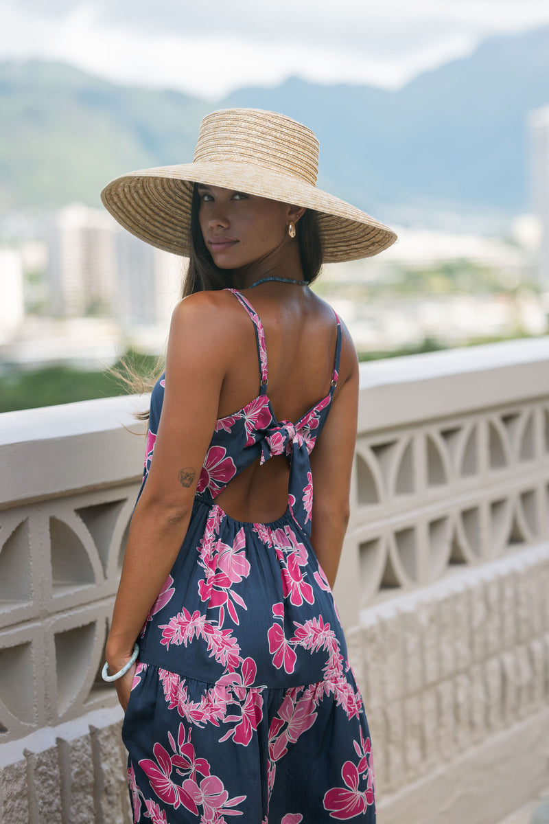 Woman wearing a dark blue sundress featuring pink ginger flowers and lei.