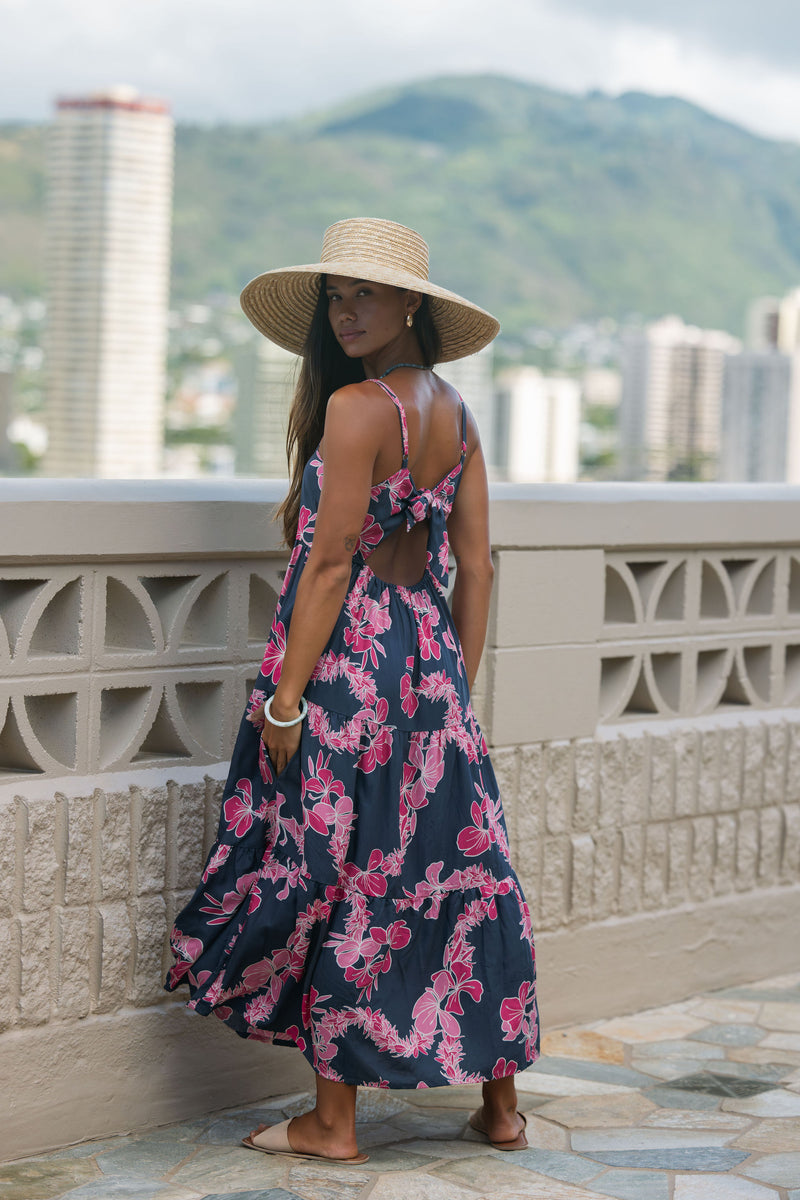 Woman wearing a dark blue sundress featuring pink ginger flowers and lei.