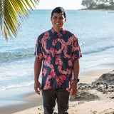 Man in button up shirt with dark navy ground and pink ginger and lei.