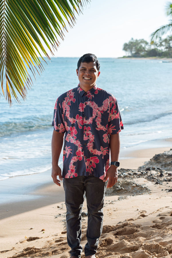 Man in button up shirt with dark navy ground and pink ginger and lei.