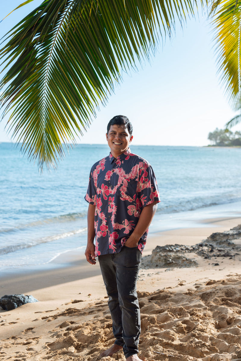 Man in button up shirt with dark navy ground and pink ginger and lei.