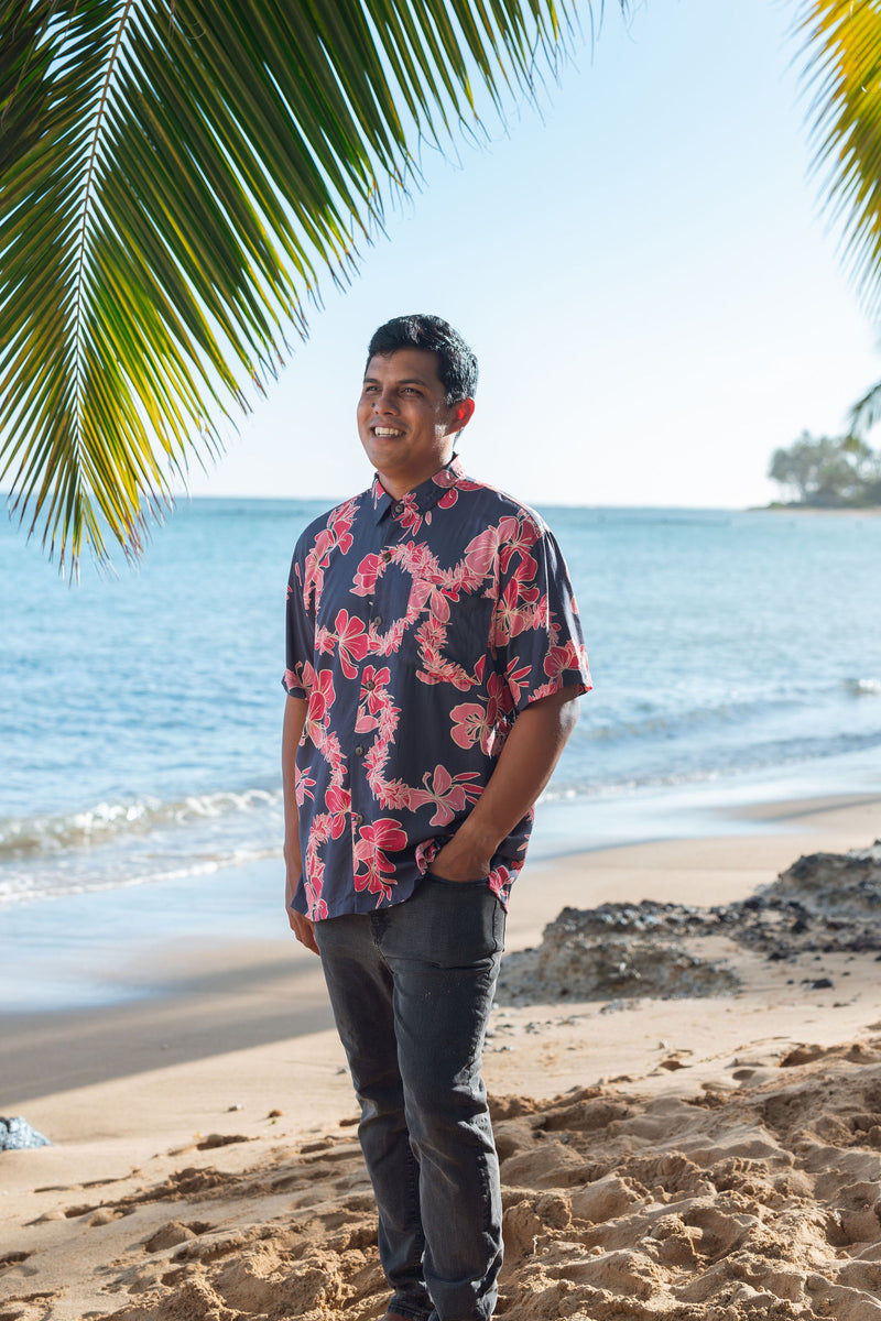 Man in button up shirt with dark navy ground and pink ginger and lei.