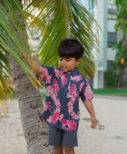 Boy in button up shirt with dark navy ground and pink ginger and lei.