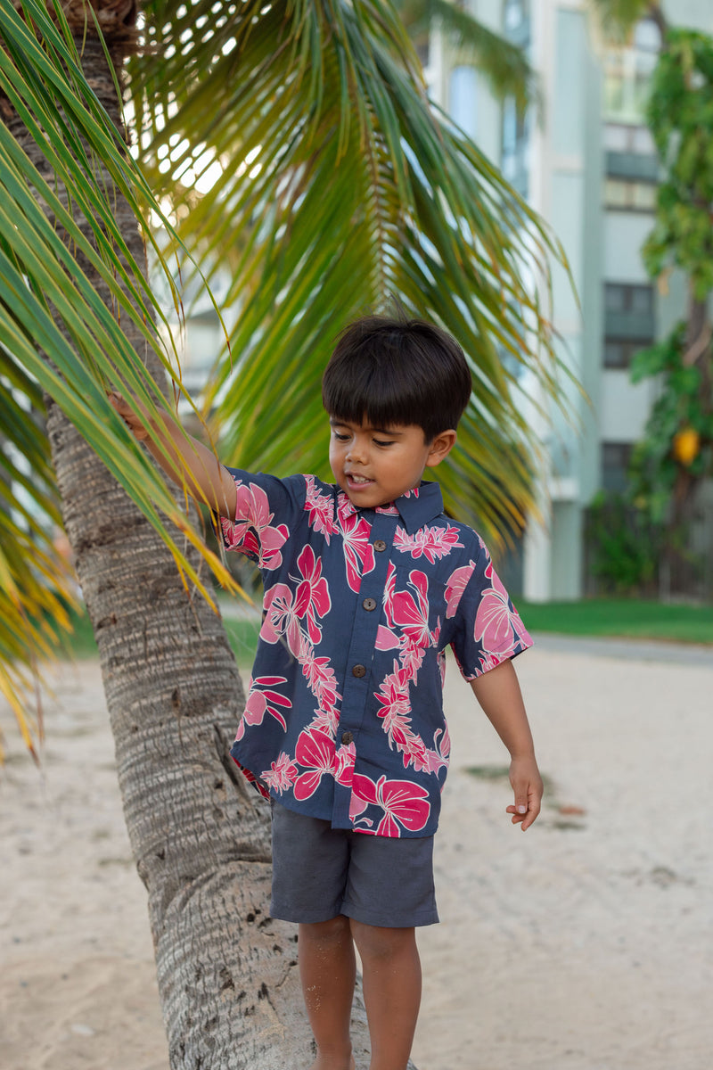 Boy in button up shirt with dark navy ground and pink ginger and lei.