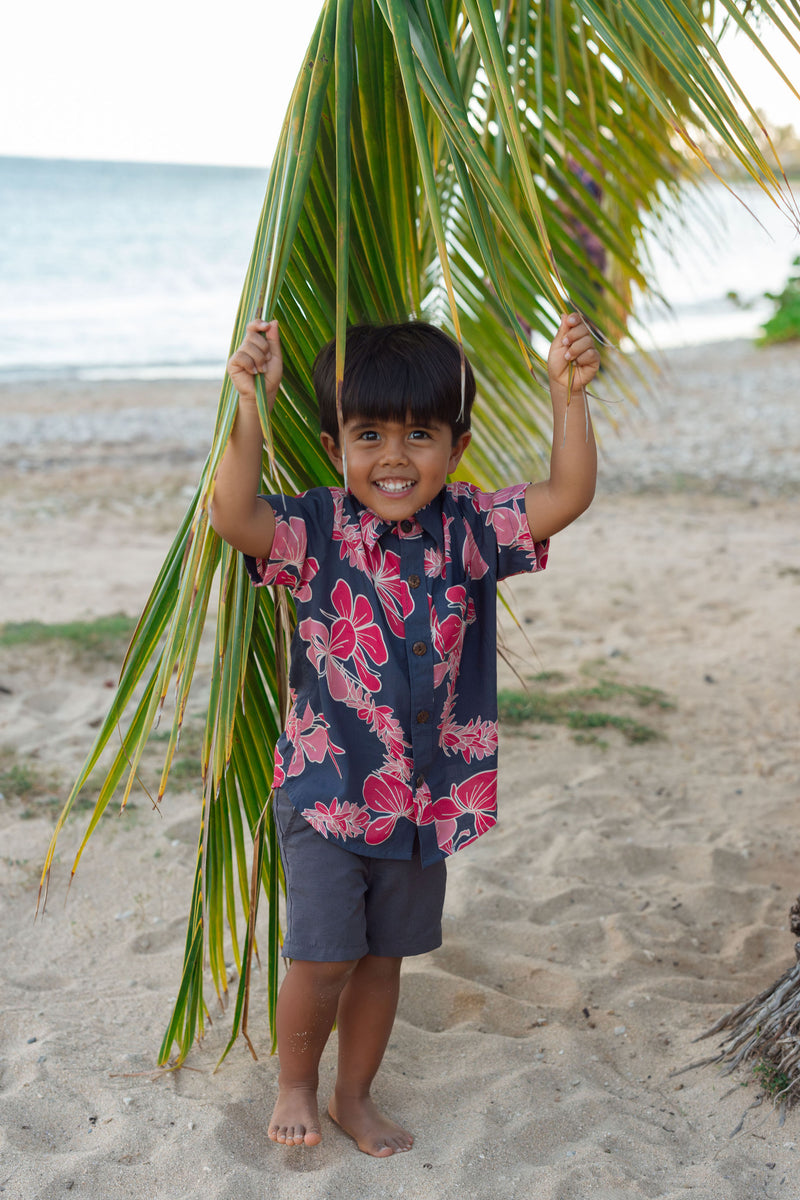 Boy in button up shirt with dark navy ground and pink ginger and lei.