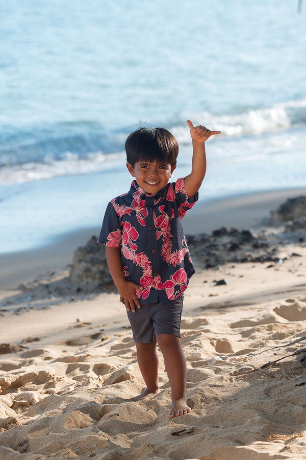 Boy in button up shirt with dark navy ground and pink ginger and lei.