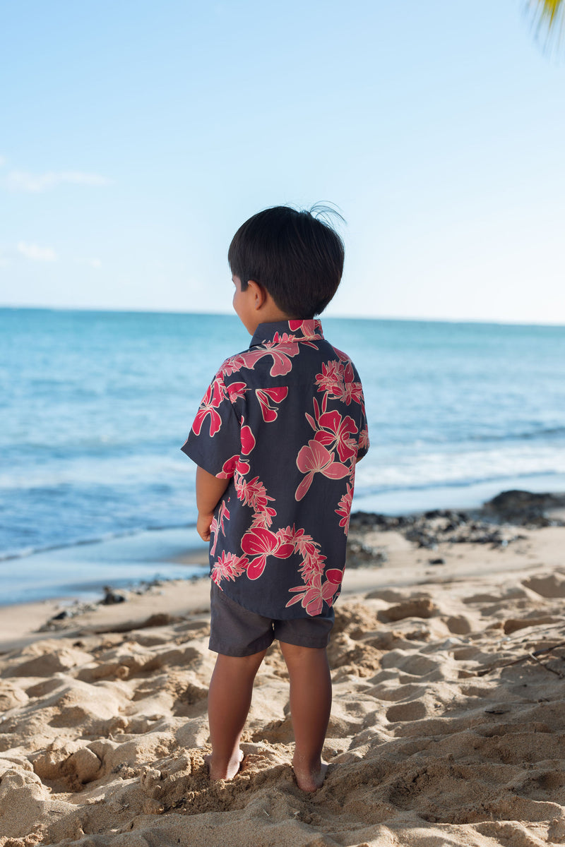 Boy in button up shirt with dark navy ground and pink ginger and lei.