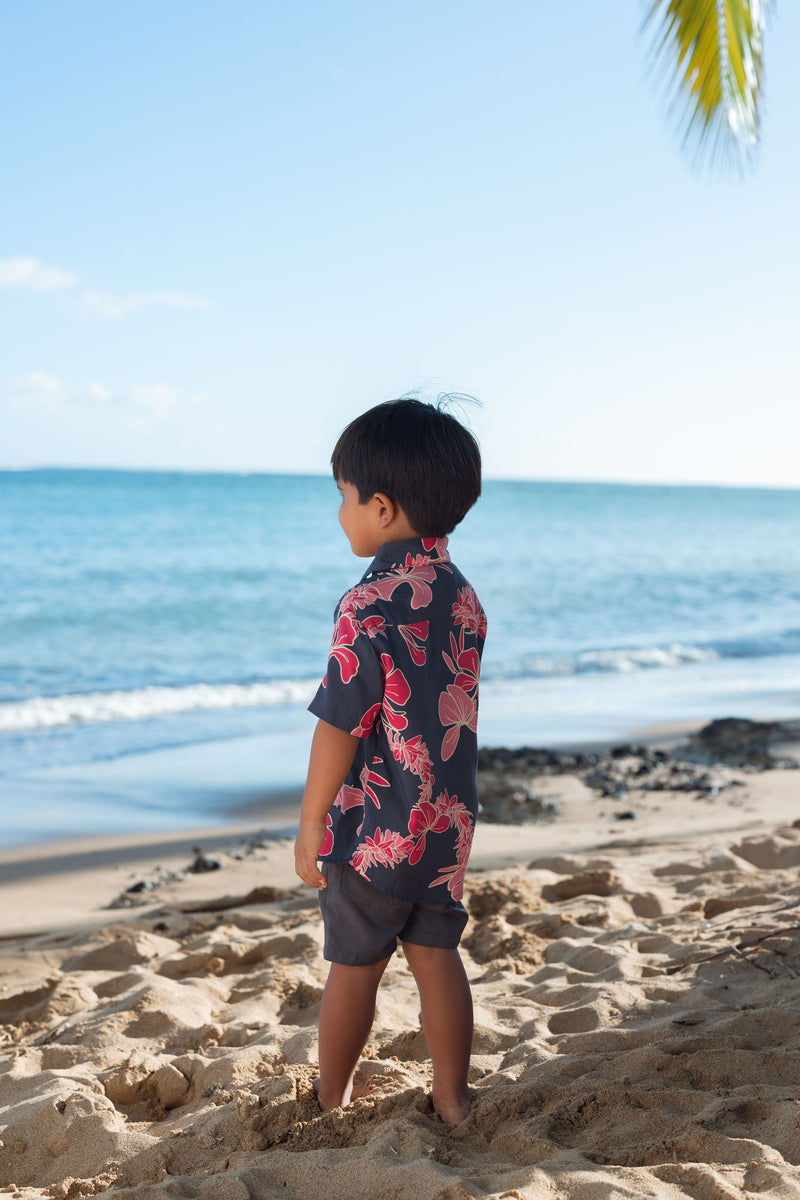 Boy in button up shirt with dark navy ground and pink ginger and lei.