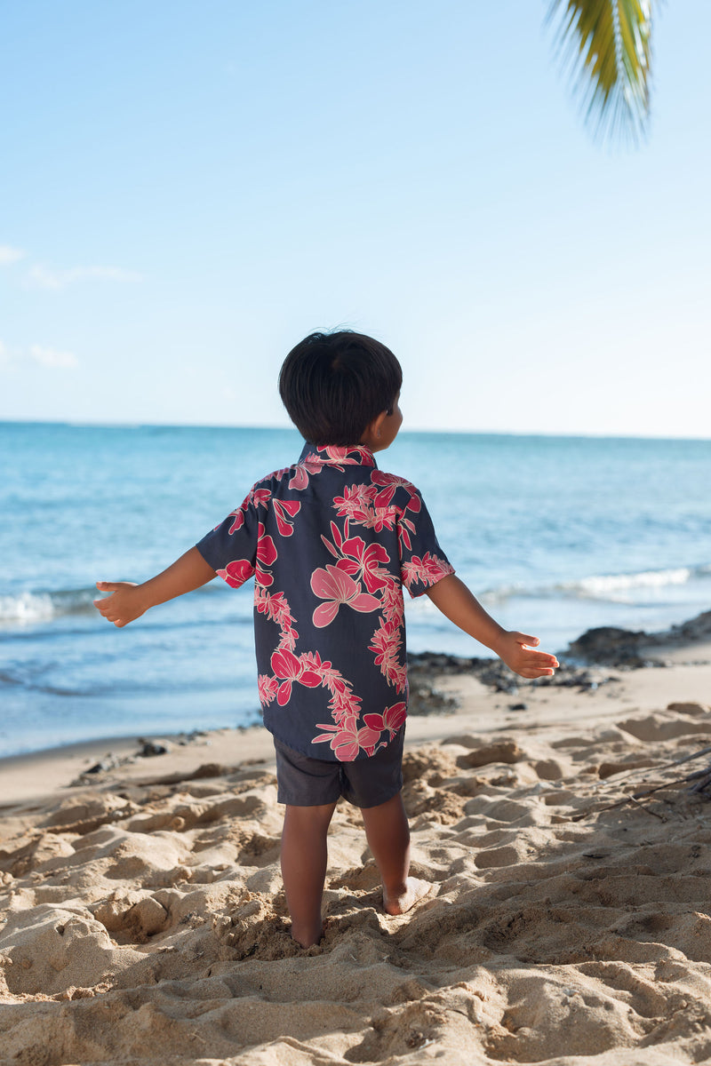 Boy in button up shirt with dark navy ground and pink ginger and lei.