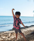 Boy in button up shirt with dark navy ground and pink ginger and lei.