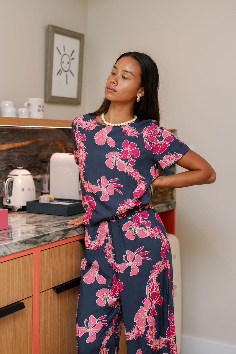 Woman wearing top and pants in navy with pink ginger and lei print.