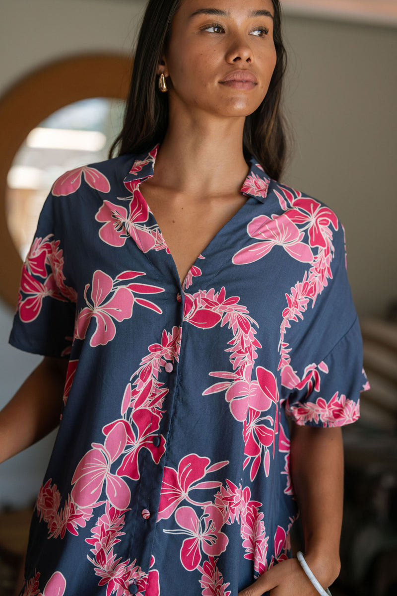 Woman in an above the knee shirt dress with dark navy ground and pink ginger and lei print.