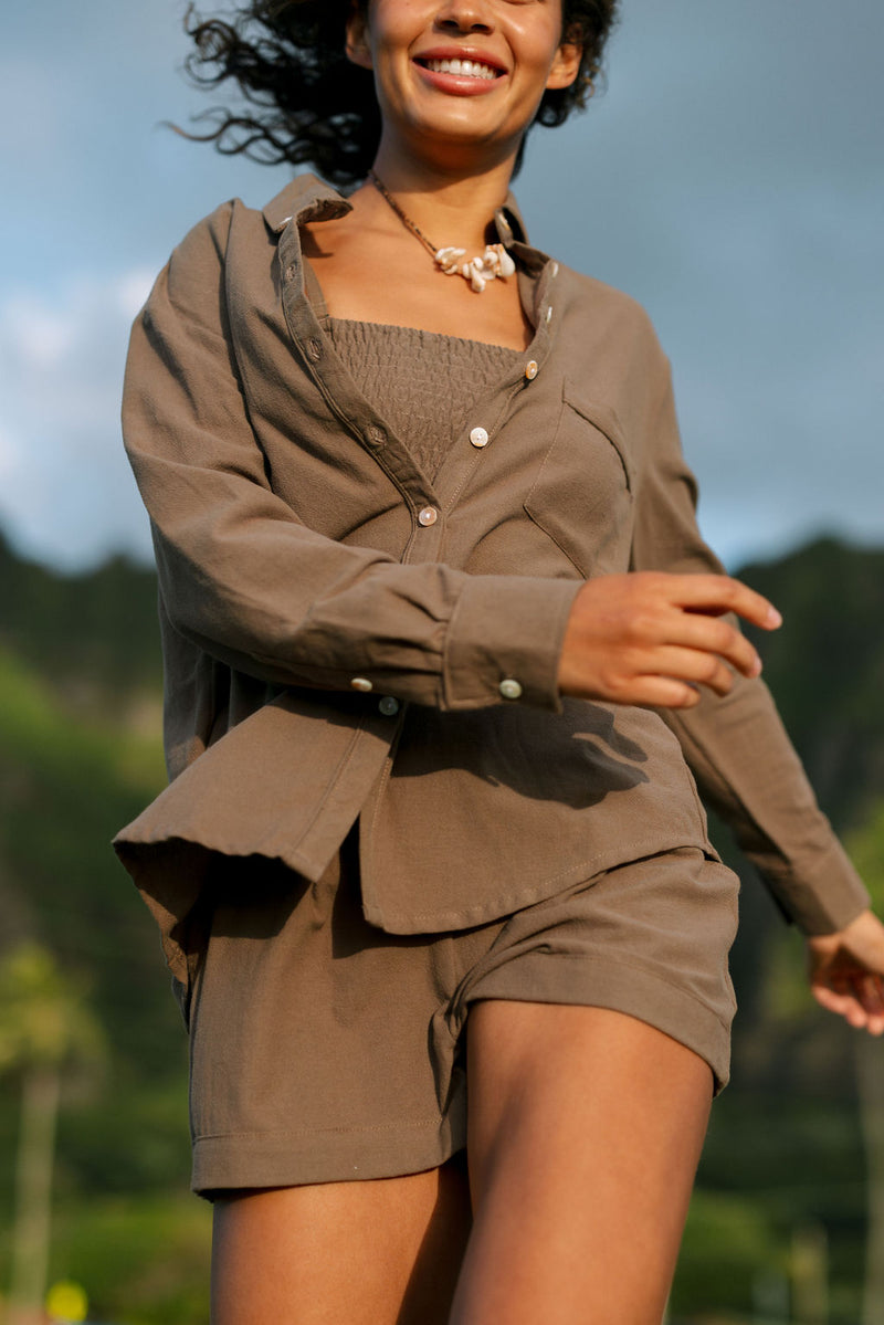 Woman wearing loose button up, smocked tube top and short in medium brown linen.