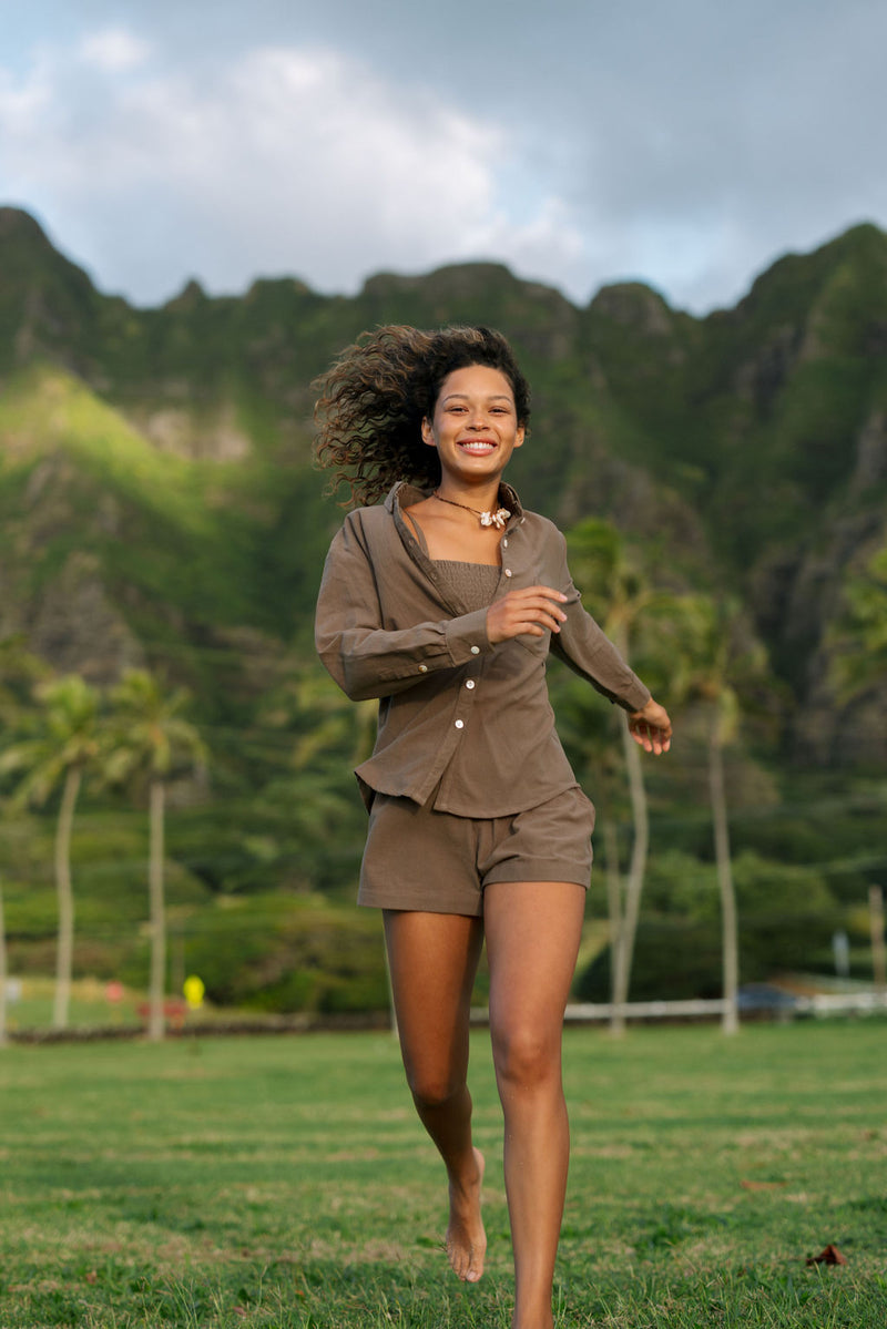 Woman wearing loose button up, smocked tube top and short in medium brown linen.