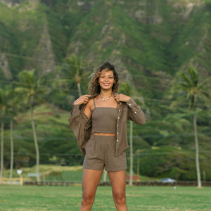 Woman wearing loose button up, smocked tube top and short in medium brown linen.