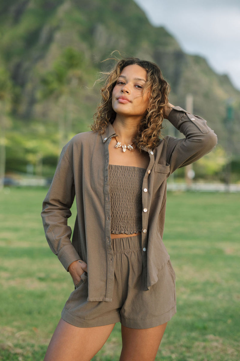 Woman wearing loose button up, smocked tube top and short in medium brown linen.