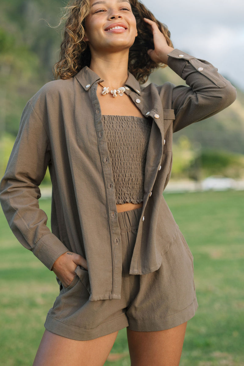 Woman wearing loose button up, smocked tube top and short in medium brown linen.