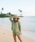 Woman wearing loose button up with smocked tube top and short in medium green linen.