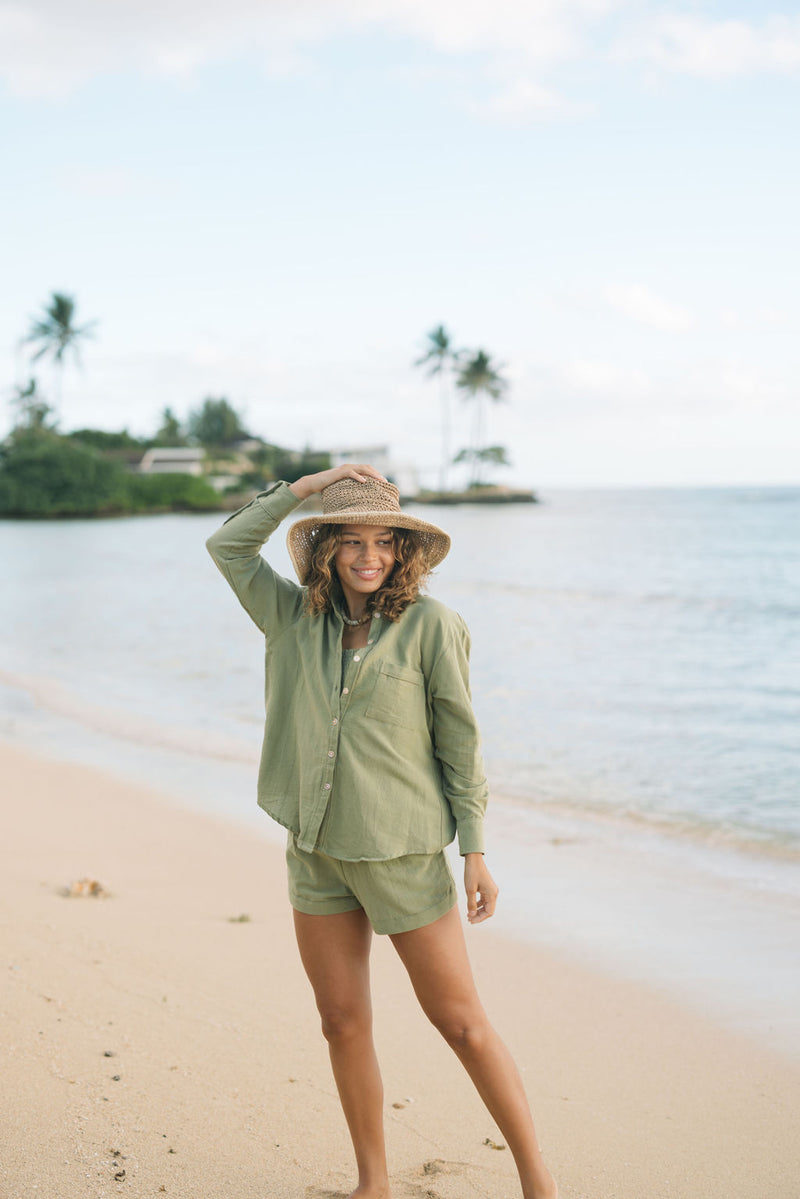 Woman wearing loose button up with smocked tube top and short in medium green linen.