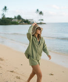 Woman wearing loose button up with smocked tube top and short in medium green linen.