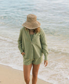 Woman wearing loose button up with smocked tube top and short in medium green linen.