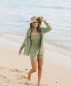 Woman wearing loose button up with smocked tube top and short in medium green linen.