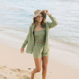 Woman wearing loose button up and smocked tube top with spaghetti straps and short in medium green linen.