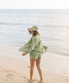 Woman wearing loose button up with smocked tube top and short in medium green linen.