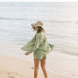 Woman wearing loose button up and smocked tube top with spaghetti straps and short in medium green linen.