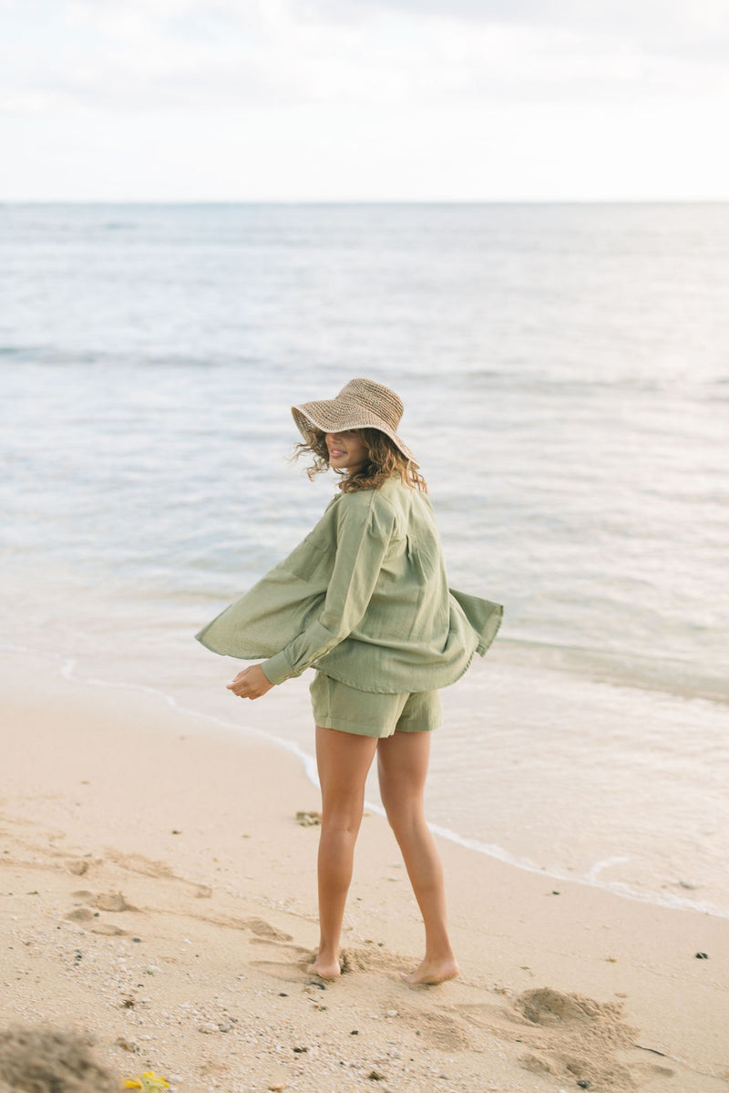 Woman wearing loose button up and smocked tube top with spaghetti straps and short in medium green linen.