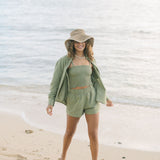 Woman wearing loose button up and smocked tube top with spaghetti straps and short in medium green linen.
